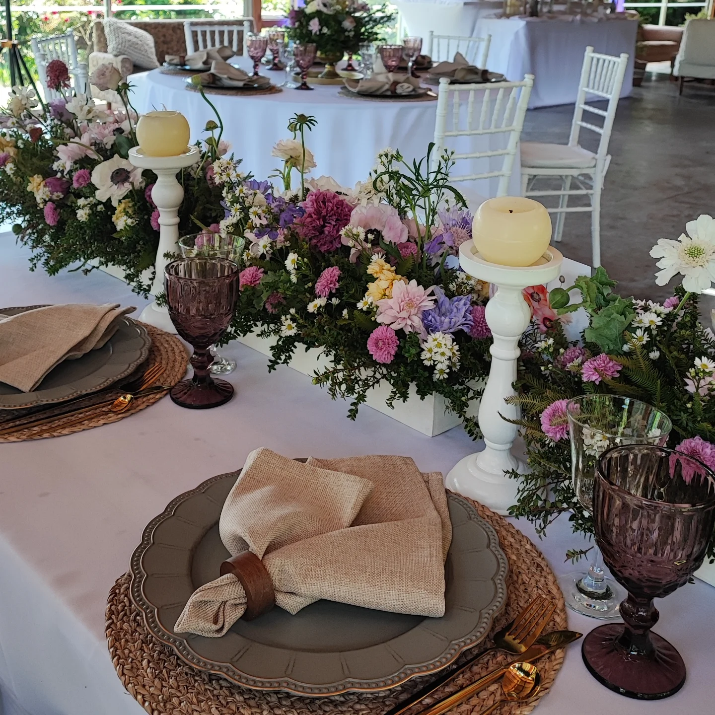 Grand dramatic floral arch installation framing a scenic outdoor ceremony space at sunset with warm golden light